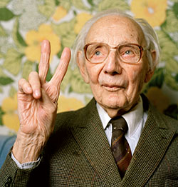 An elderly man puts his fingers up in a victory sign.

